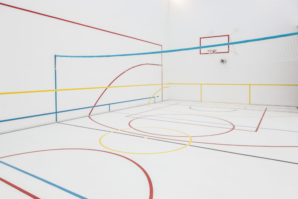 A white gallery space is marked out with colourful lines like a sports hall