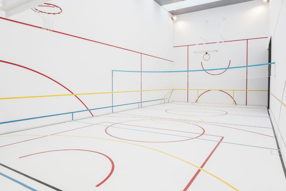 A white gallery space is marked out with colourful lines like a sports hall