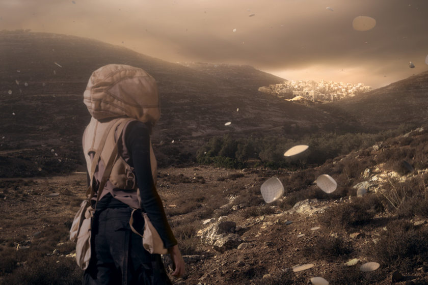 Film still of a figure wearing a hooded jacket looking out towards a hilly landscape with a bright city in far the distance, porcelain type objects float in the air around her