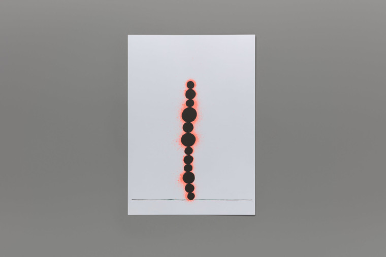 Upon a thin black line that crosses the width of the page 12 black circles of different sizes are stacked on top of each other with neon orange spray painted circles behind them. The edition is photographed on a grey background.