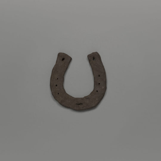 Hand crafted horseshoe in dark clay, photographed against a grey background.