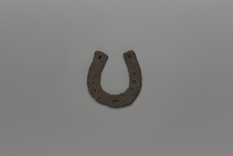 Hand crafted horseshoe in dark clay, photographed against a grey background.