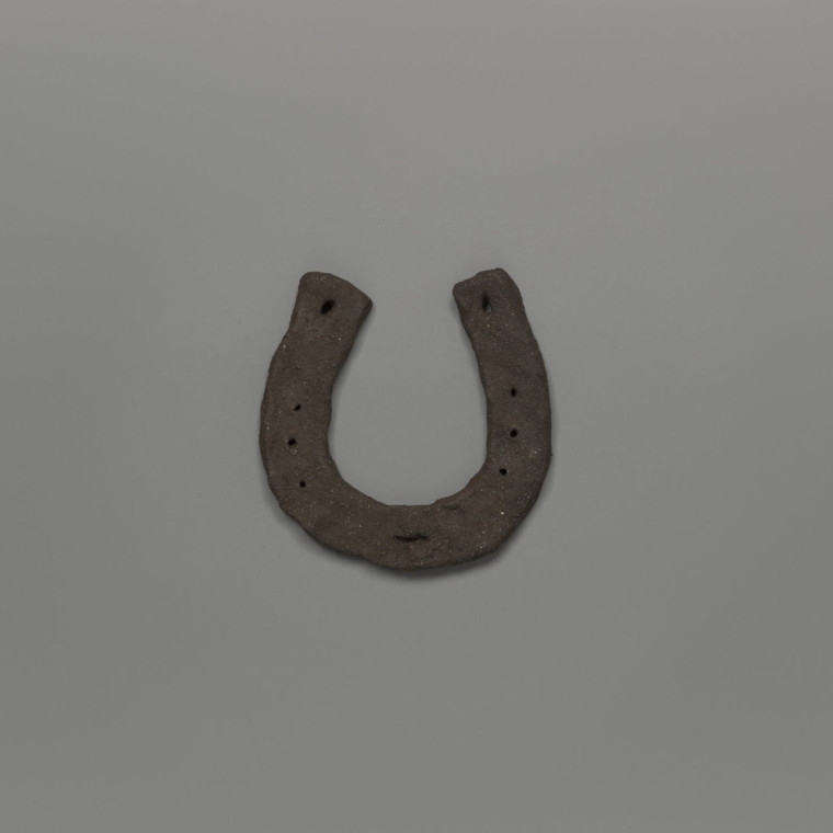 Hand crafted horseshoe in dark clay, photographed against a grey background.