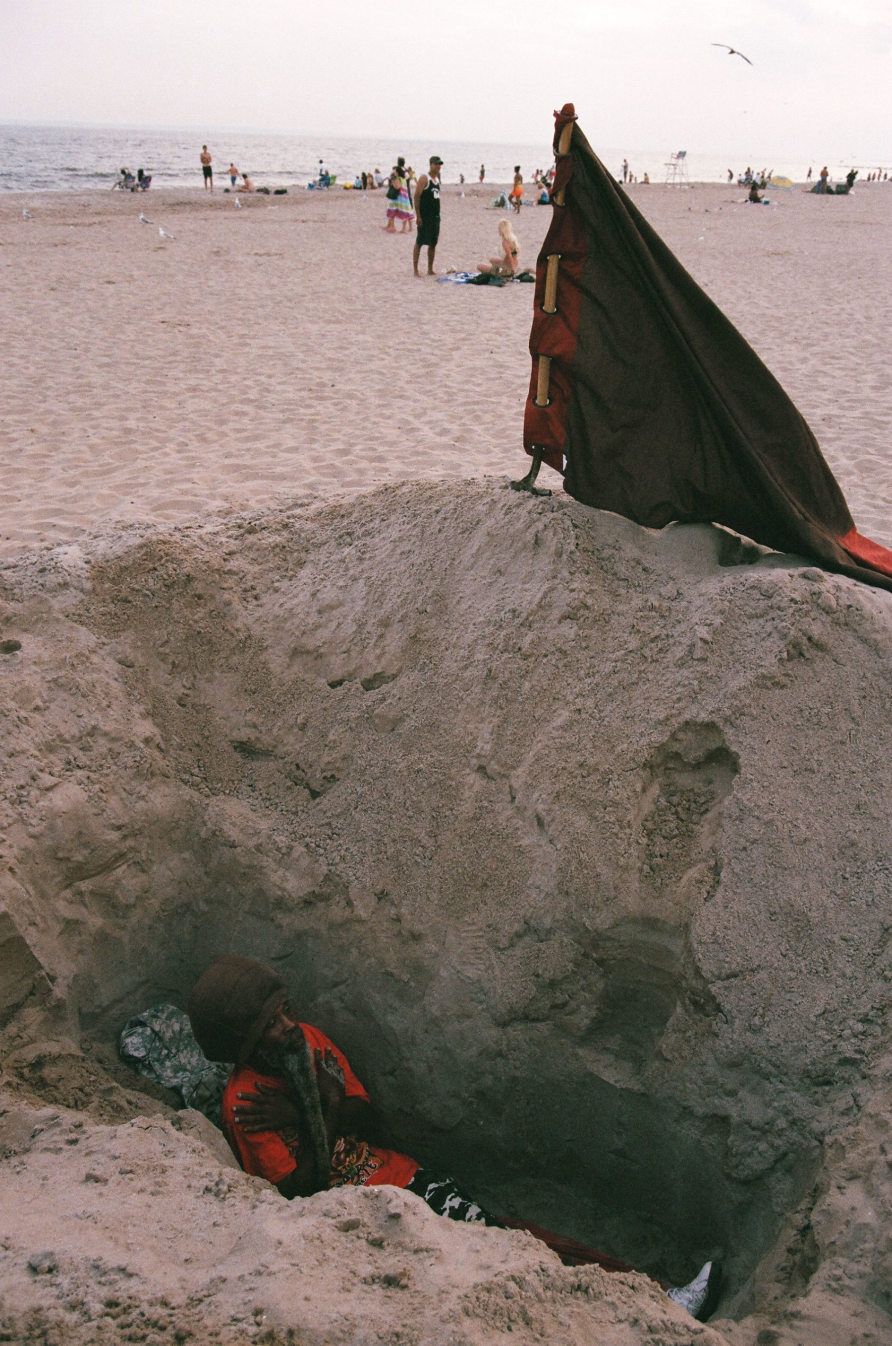 A photograph of a man down a hole on a sandy beach, the top of his head and torso is just visible.