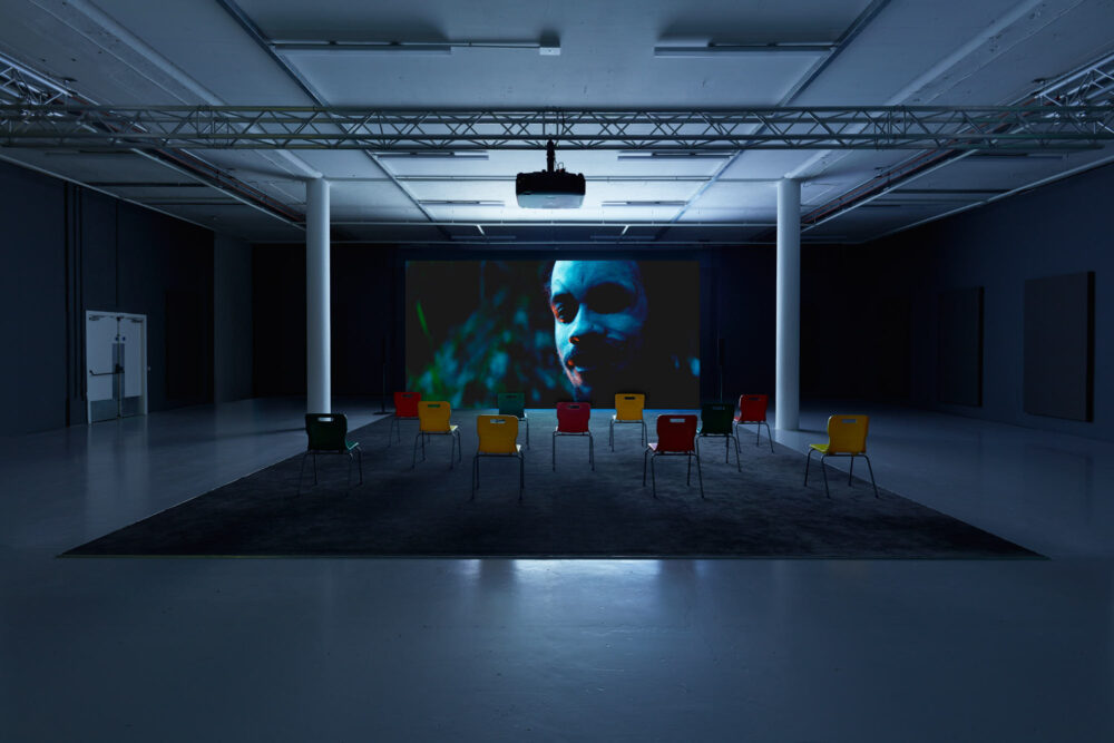 Gallery view of a projection screen showing a close up of a man wearing ceremonial face paint.