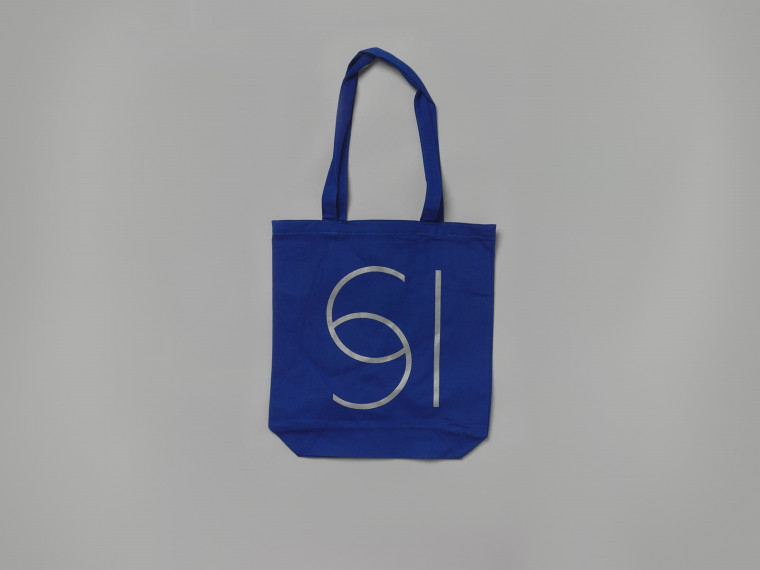 A photograph of a blue tote bag against a grey background