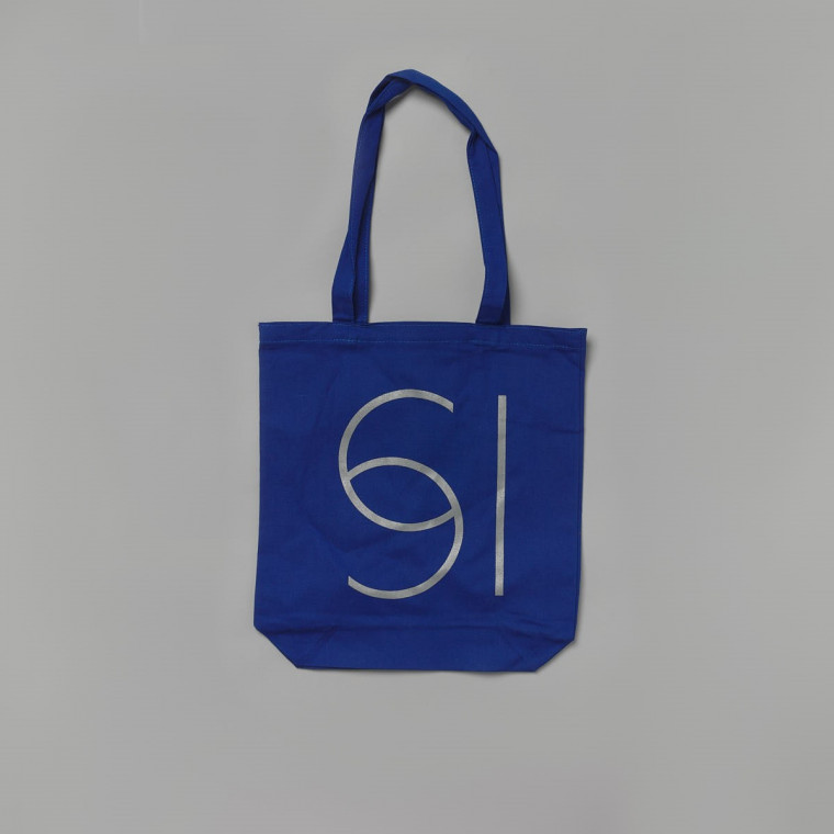 A photograph of a blue tote bag against a grey background