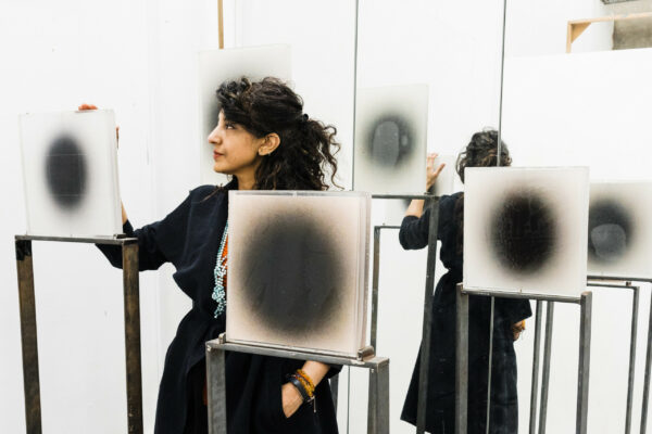 Artist Bea Kayani in her studio at Spike Island surrounded by square white panels positioned on metal frames, each has a faded black circular mark in its centre.