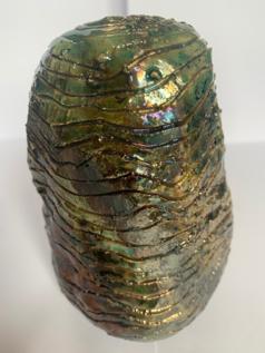 An image of a tall and round ceramic object with lines carved into the clay and a metallic green glaze.