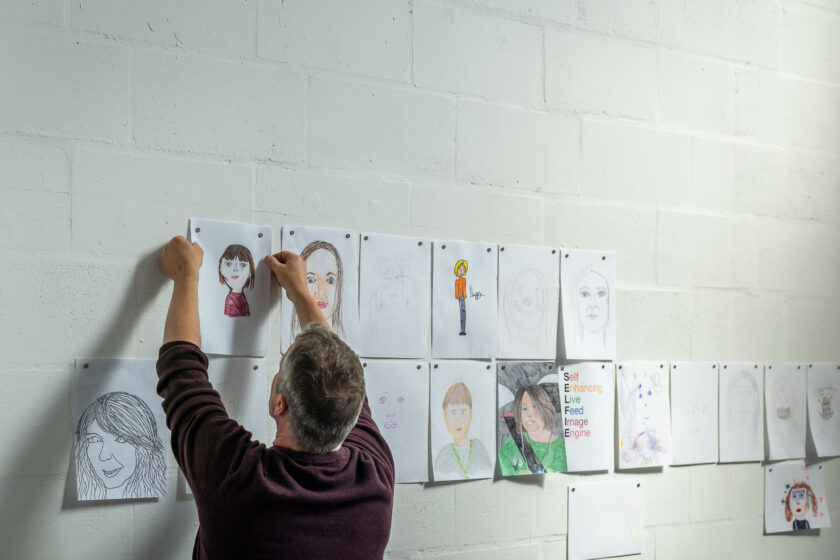 A white man with dark hair putting up pictures on a white wall