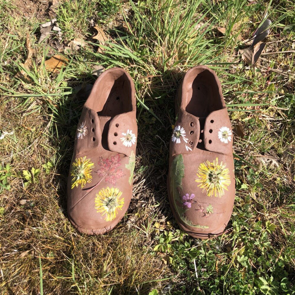 A pair of clay shoes with flowers pressed into them, sitting on grass