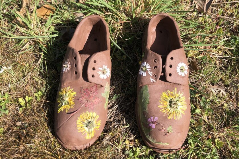 A pair of clay shoes with flowers pressed into them, sitting on grass