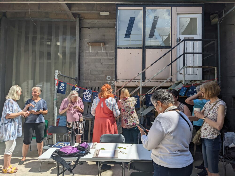 A photograph of adult women talking pinning art on a washing line.