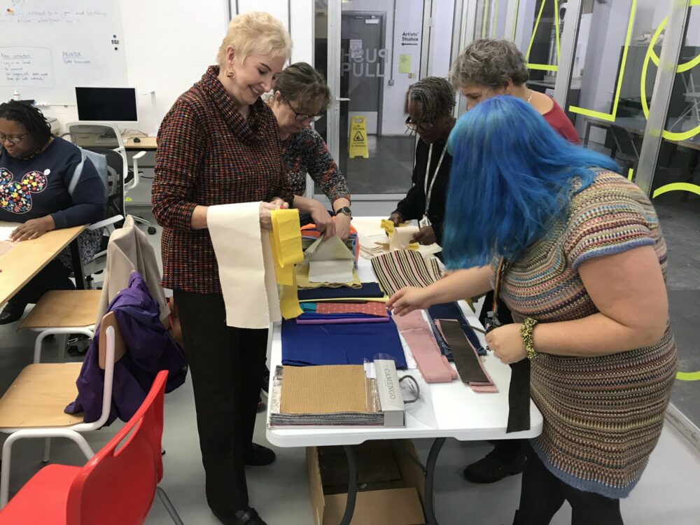 A photograph of a group of women look at fabrics.