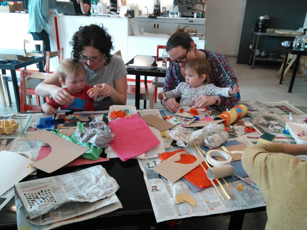 Photograph of two adults crafting with their infants at a crafting table.