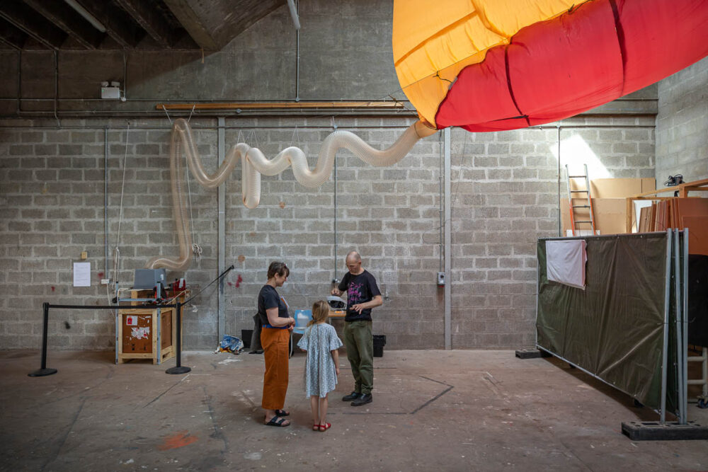 A photograph of two adults and a child standing underneath a balloon-like blow up structure.