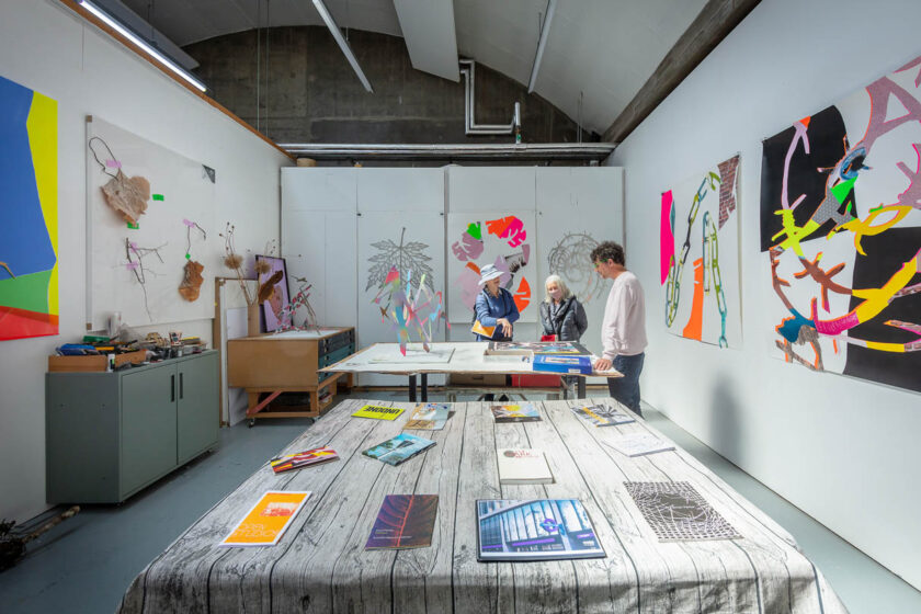 A photograph of a studio with three people standing around a table looking at prints.