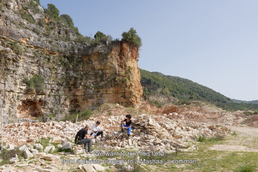 A film still showing three people sitting on rocks in an open rural landscape.