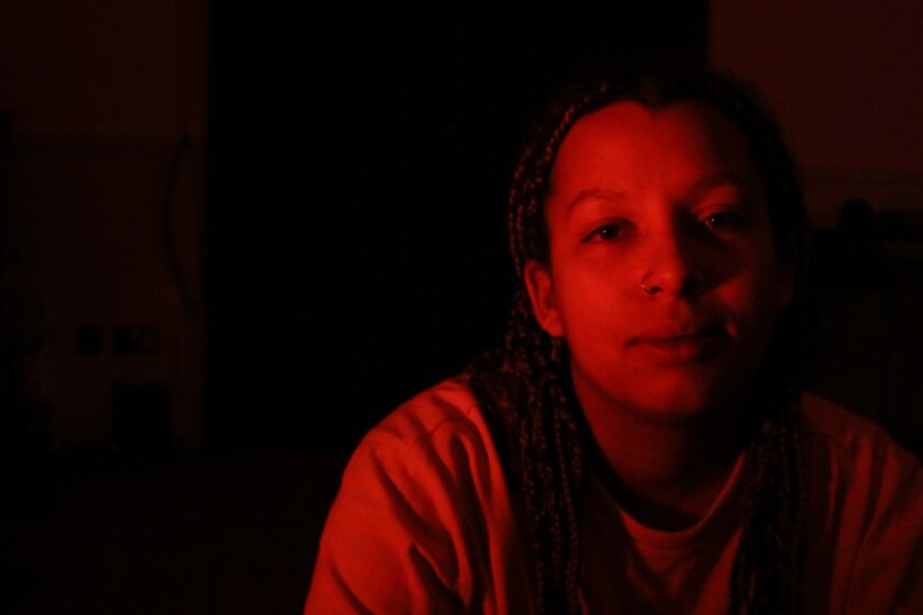 Portrait image of Ama Dogbe in dark room with coloured lighting.