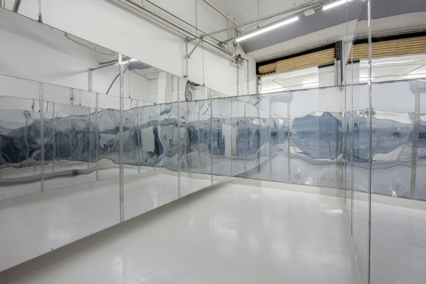 A photograph of an installation of three walls of mirrors showing distorted and transparent reflections.