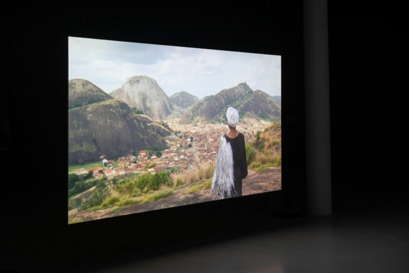 A film screen showing a woman looking out over the Idanre Hills hangs in a dark gallery.