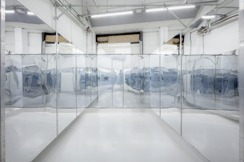 Interior of a mirrored pavilion suspended from the ceiling in a white gallery space.