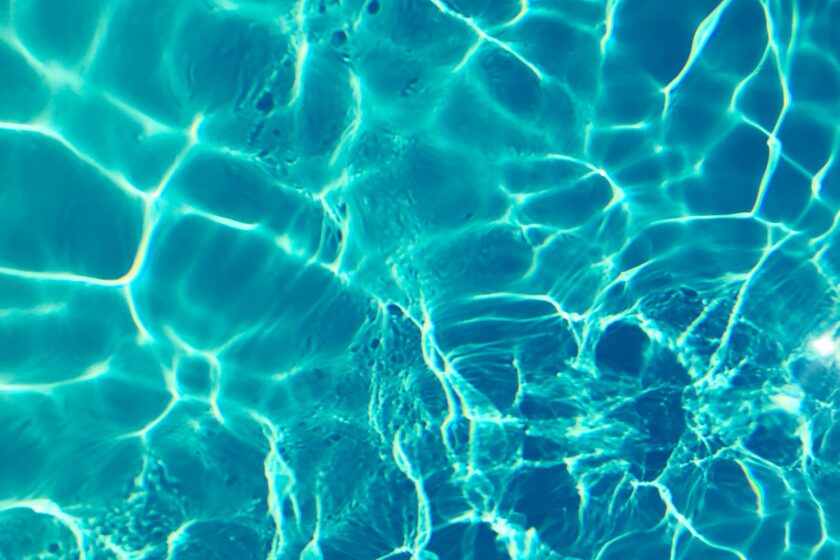 A cyan blue close up of water in a swimming pool with sunny reflections.