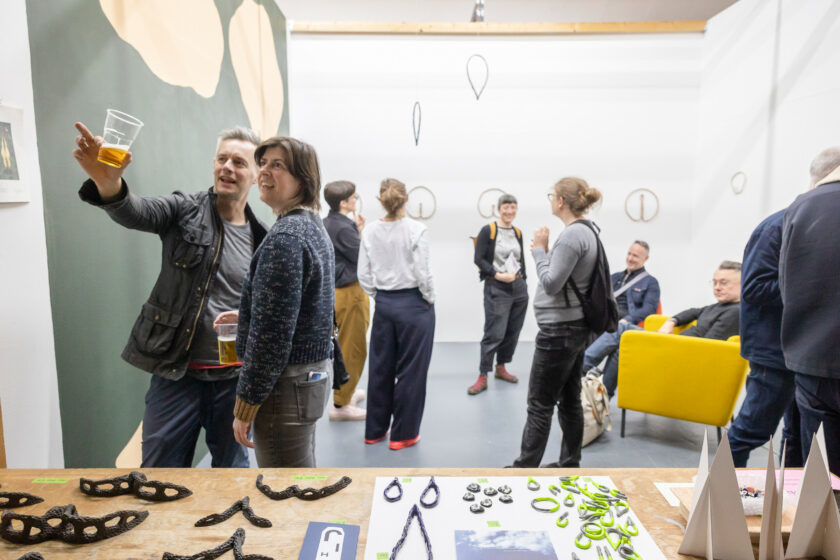 Two people in foreground smiling and pointing at art inside of a studio with three people in the background.