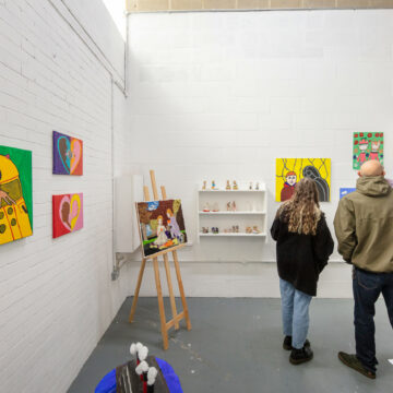 Two people on right hand of photo backs turned looking at art in an artists studio.