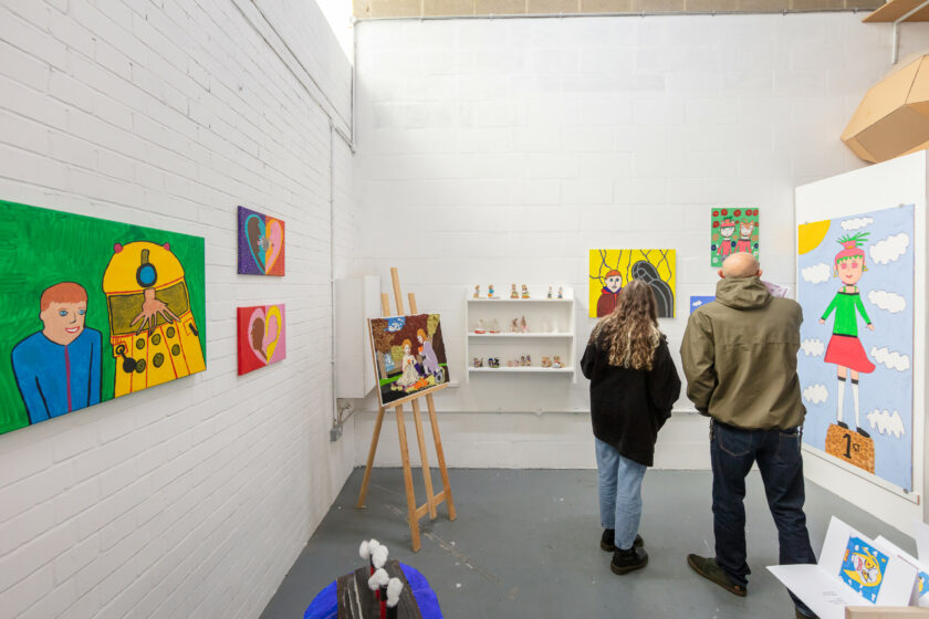 Two people on right hand of photo backs turned looking at art in an artists studio.