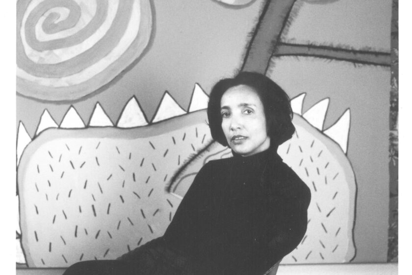 A black and white photograph of the artist Ofelia Rodríguez sitting in front of her artwork.