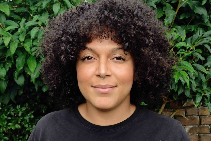 Portrait image of a woman standing outside against leafy wall.