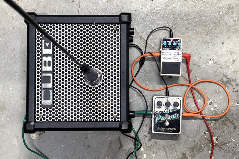 Photo of a guitar amp with audio effects pedals and a microphone attached